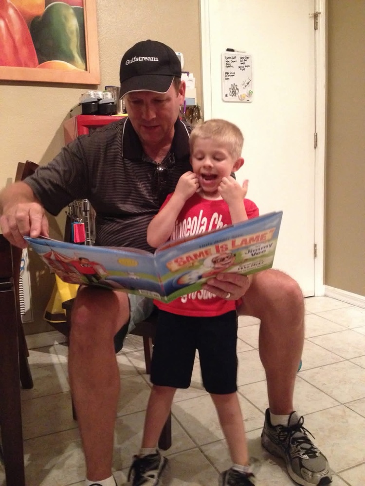 A dad reading a Jimmy Vee book to his delighted young son